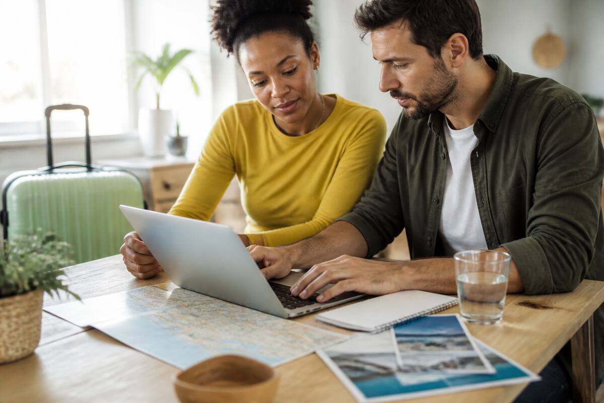 Stel vergelijkt vakanties op een laptop aan tafel met reisplanners